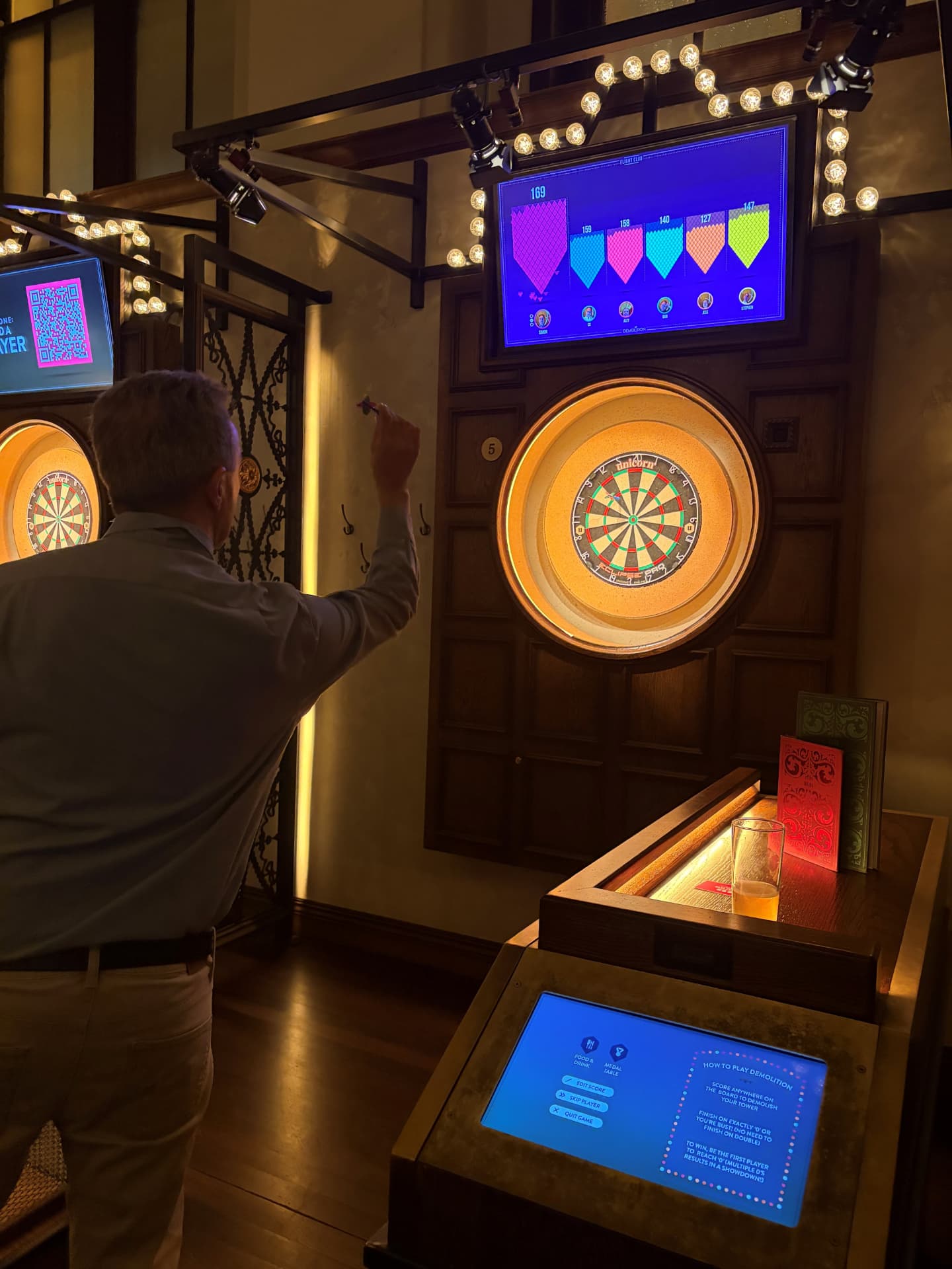 A guest throwing a dart with the live scoreboard above the board